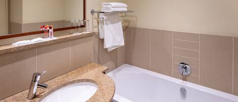 A bathroom with a granite sink, a white bathtub, a towel rack, and a mirror.