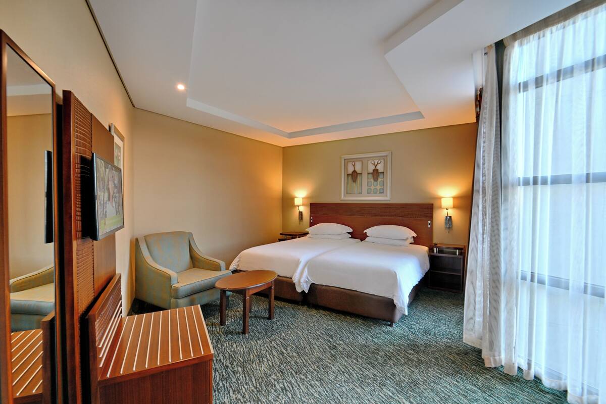 A hotel room with a bed, a chair, a small table, and a mirror.
