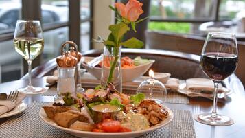 Une table à manger avec une assiette de nourriture, un verre de vin blanc, un verre de vin rouge et un vase contenant une rose.