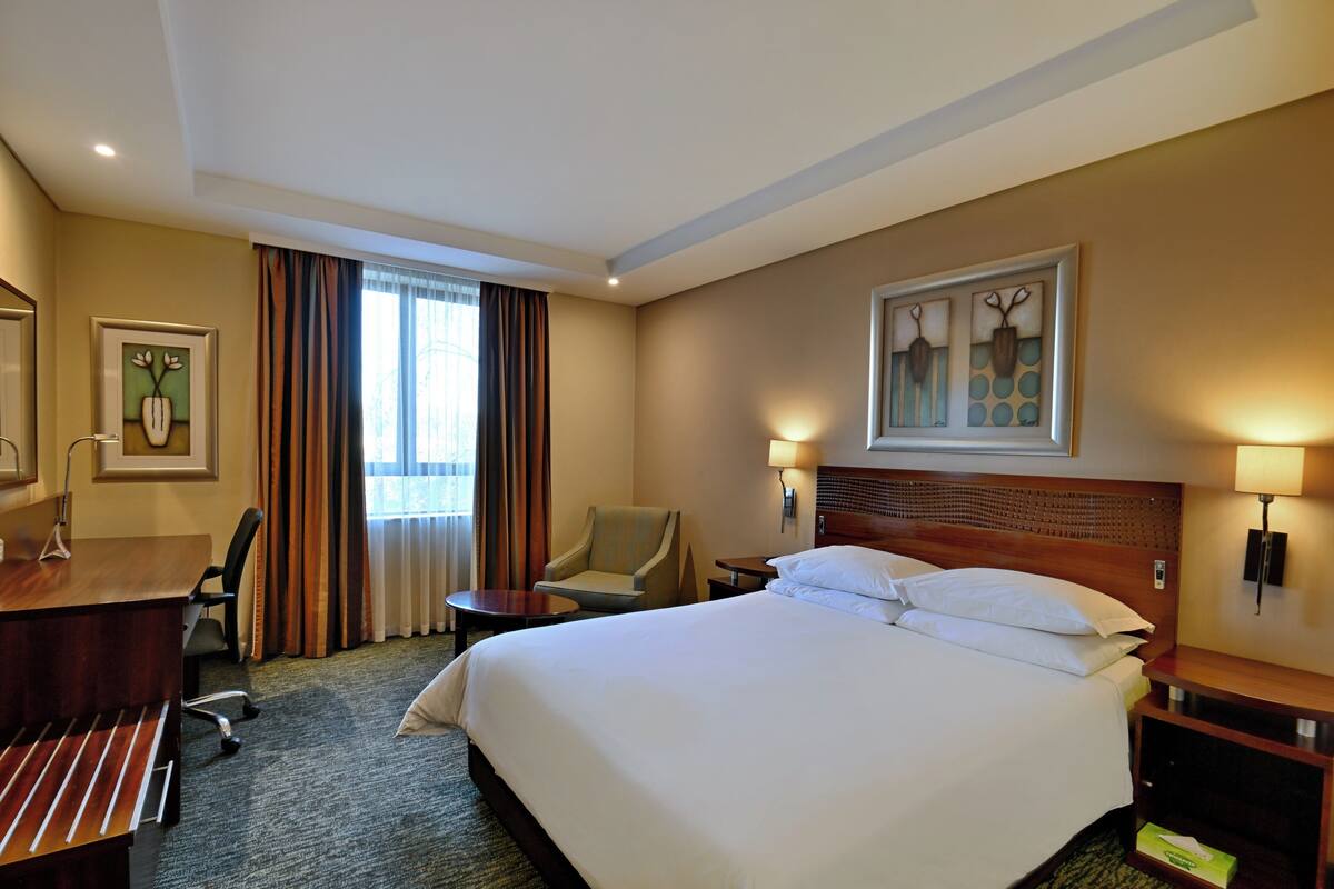 A hotel room with a large bed, a desk, a chair, and a window with curtains.