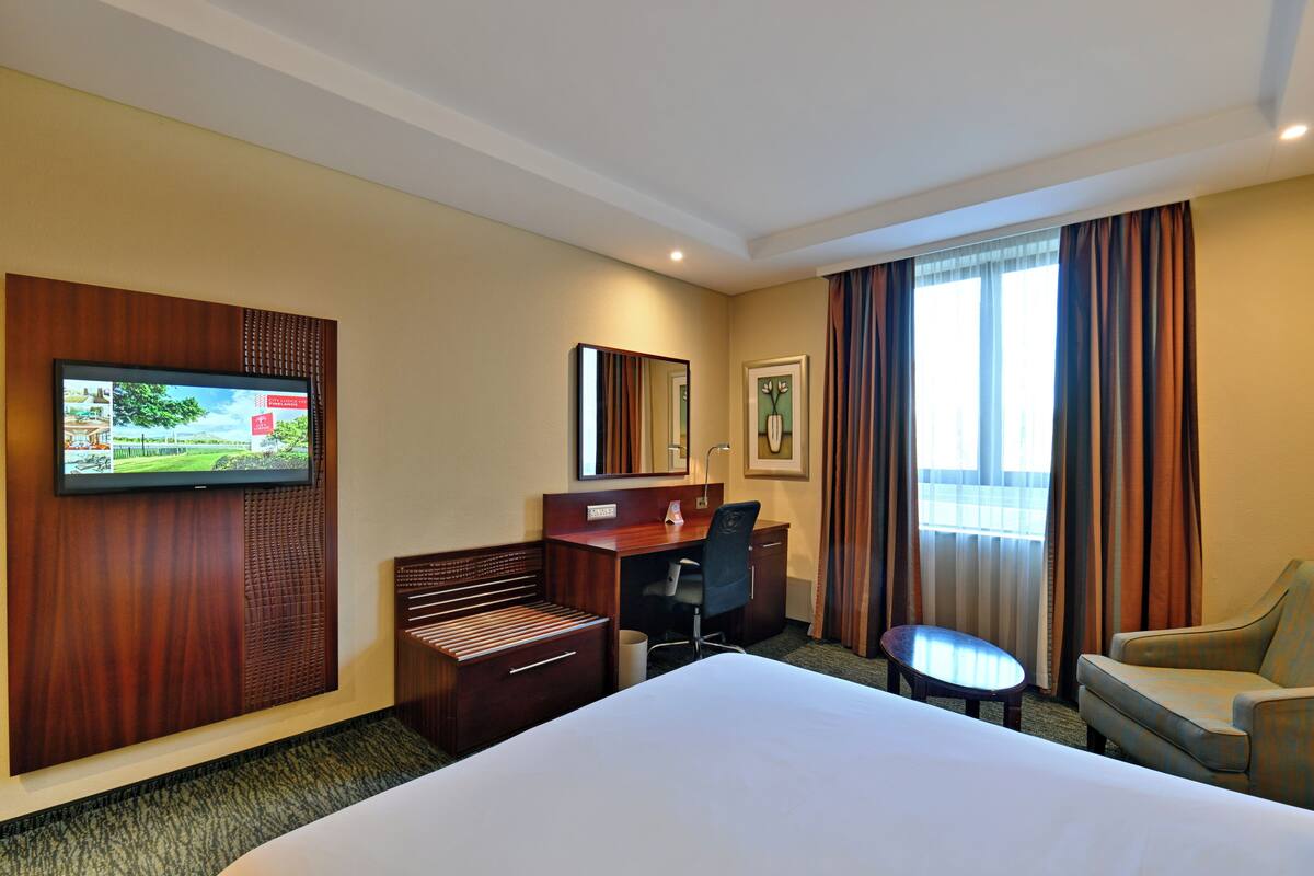 A hotel room with a bed, a desk, a chair, a television, and a window with curtains.
