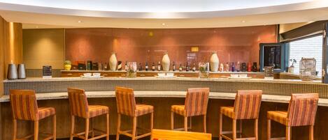 A bar area with wooden bar stools and a counter displaying various bottles.