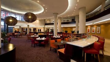 A spacious hotel lobby with multiple dining areas, large columns, and hanging spherical light fixtures.