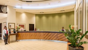 A hotel reception area with a wooden reception desk, a large potted plant, and a modern interior design. - City Lodge Hotel Hatfield (Pretoria)