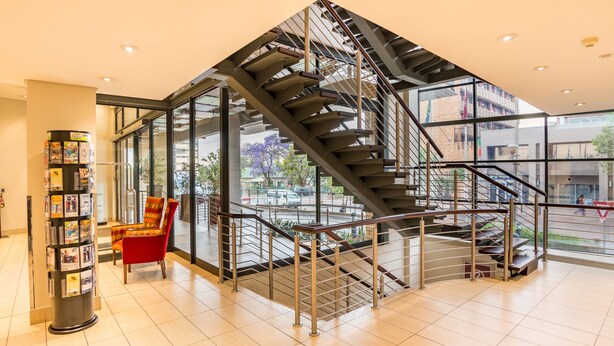 A modern interior with a spiral staircase, a red chair, and a bookcase. - City Lodge Hotel Hatfield (Pretoria)