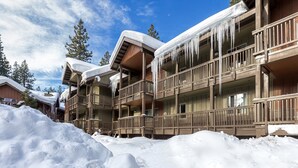 Un edificio de madera de varios pisos con balcones, cubierto de nieve y estalactitas, rodeado por un paisaje nevado.