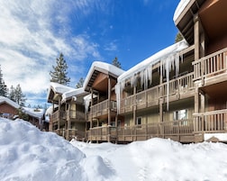 Un edificio de madera de varios pisos con balcones, cubierto de nieve y estalactitas, rodeado por un paisaje nevado.