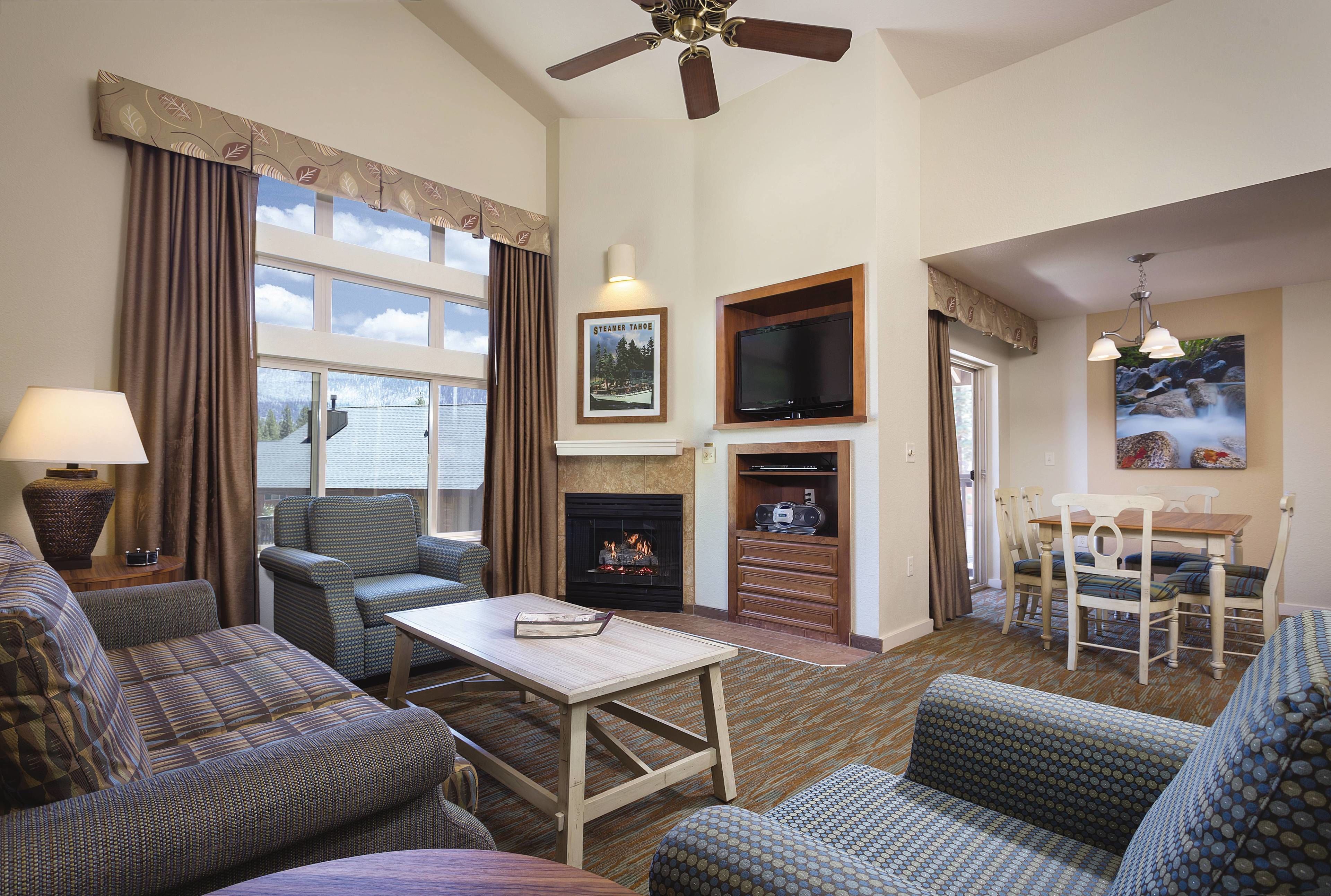 A living room with a fireplace, a television mounted above it, and a dining area with a table and chairs.