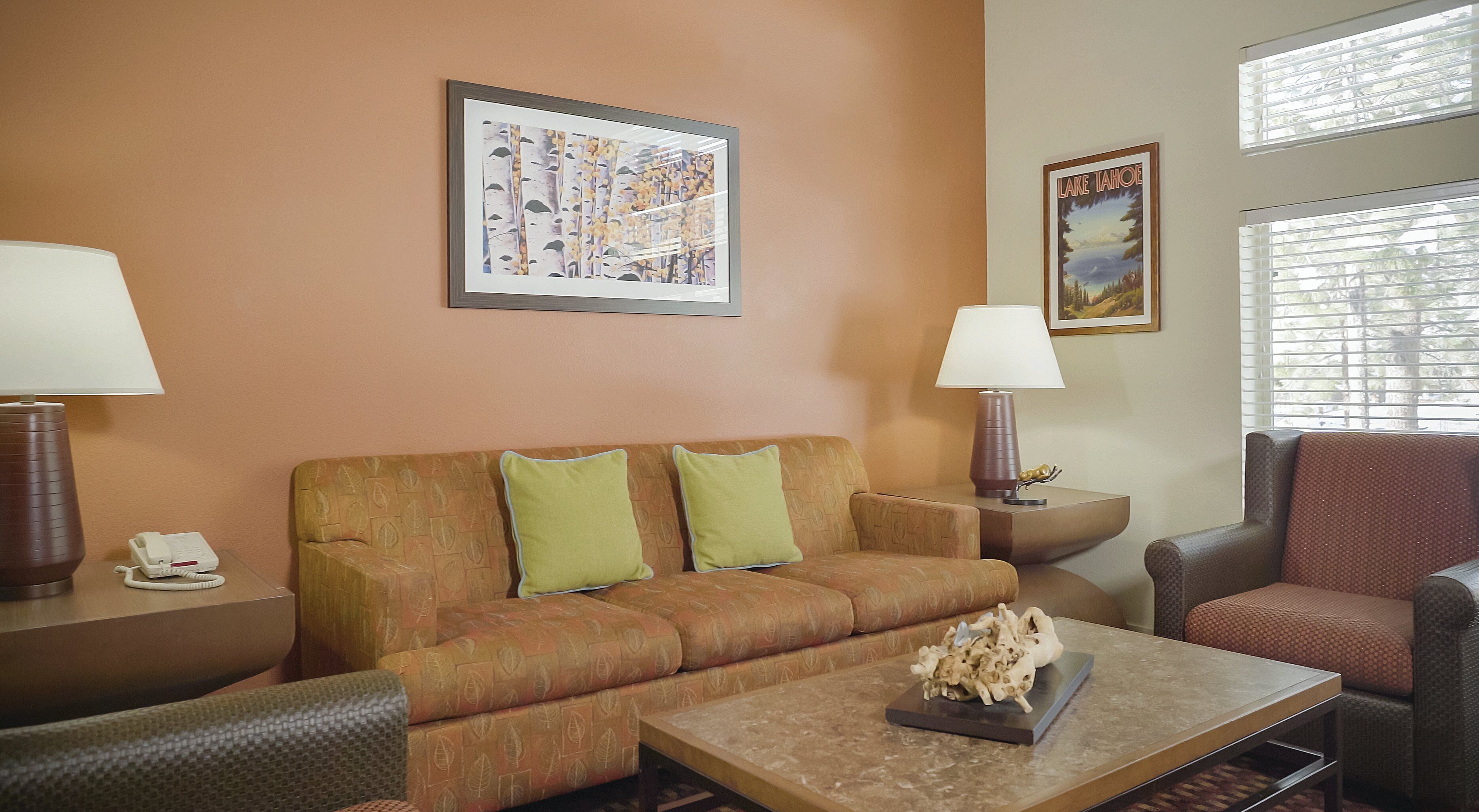 Ein Hotelzimmer mit einer Couch, zwei Sesseln, einem Couchtisch, einer Lampe, einem Telefon und zwei gerahmten Bildern an der Wand.