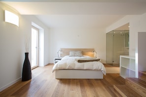 Un dormitorio moderno con una cama grande, mesitas de noche, un jarrón alto y una cabina de ducha de cristal.