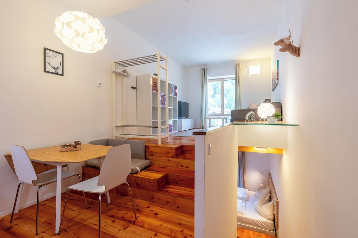 A modern living space with a wooden floor, white furniture, a staircase, and a dining area.