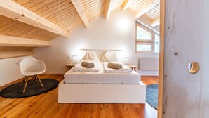 A bedroom with a wooden ceiling, a bed with pillows, a chair, and a window. - Quercus Appartements (Reichenau)