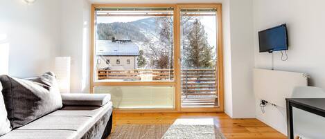 A modern living room with a sofa, a flat-screen TV, and a large window with a view of a snowy landscape.