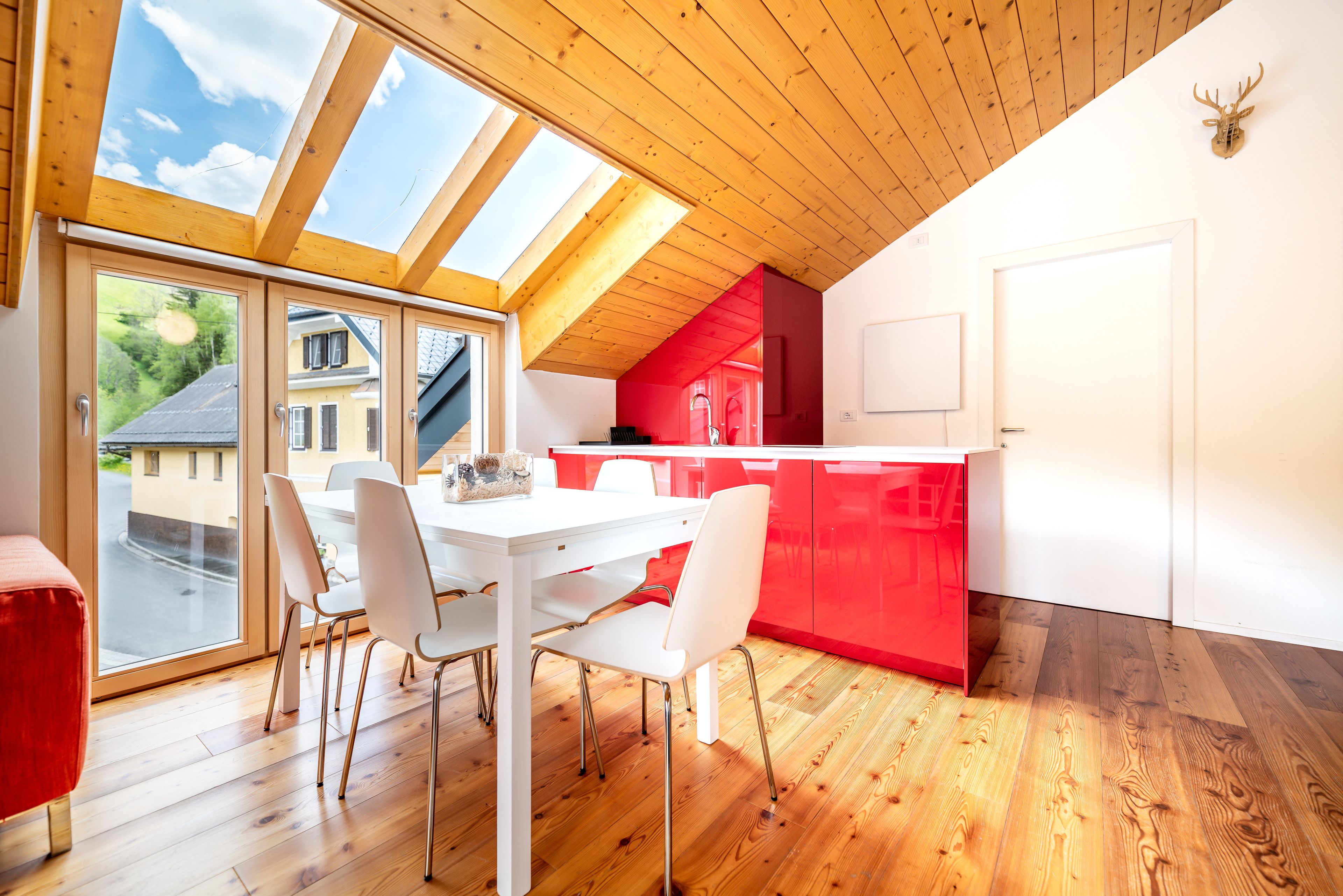 A modern kitchen with a skylight, white cabinets, and a red accent wall.