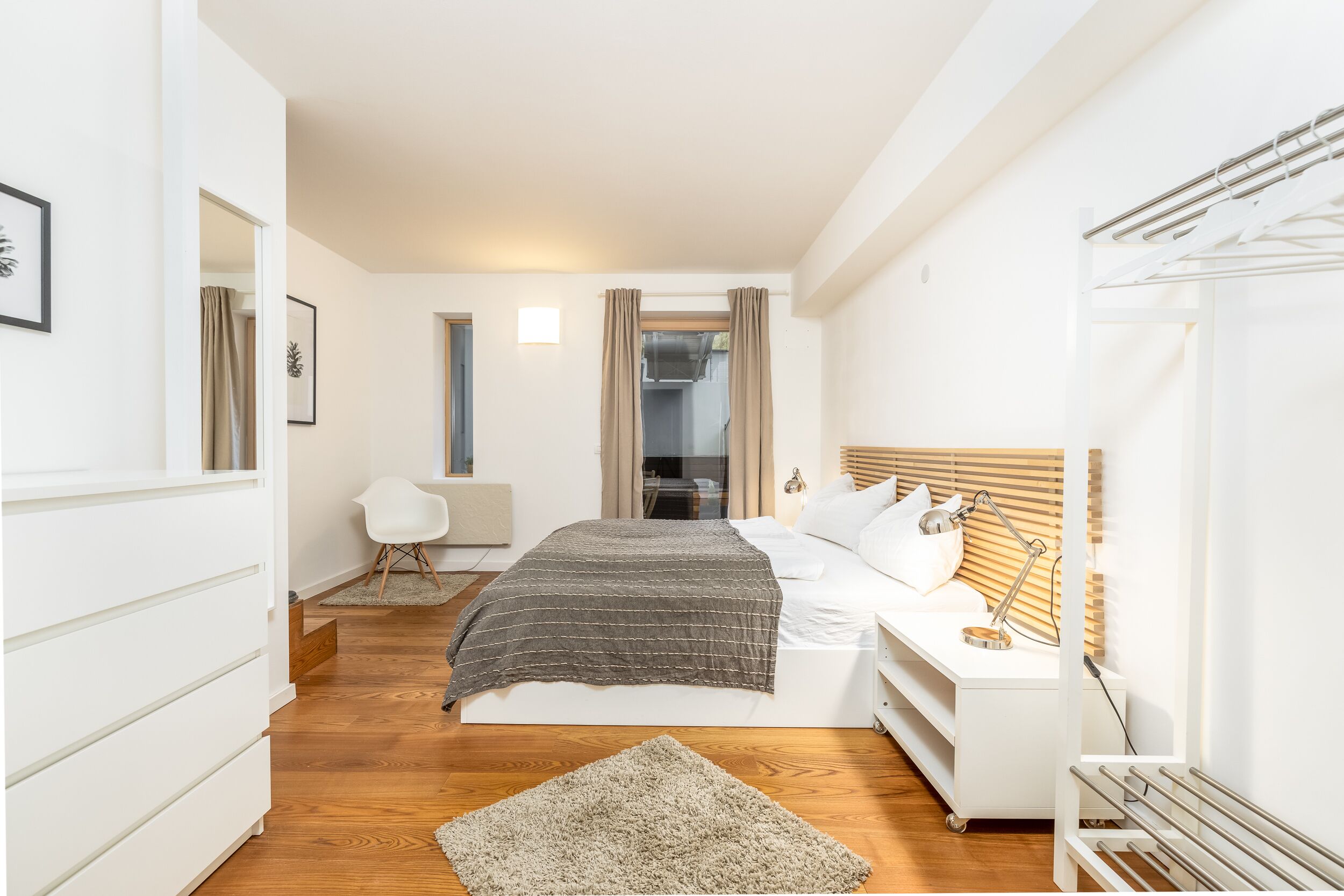 A modern bedroom with a bed, bedside table, and a small desk with a lamp.