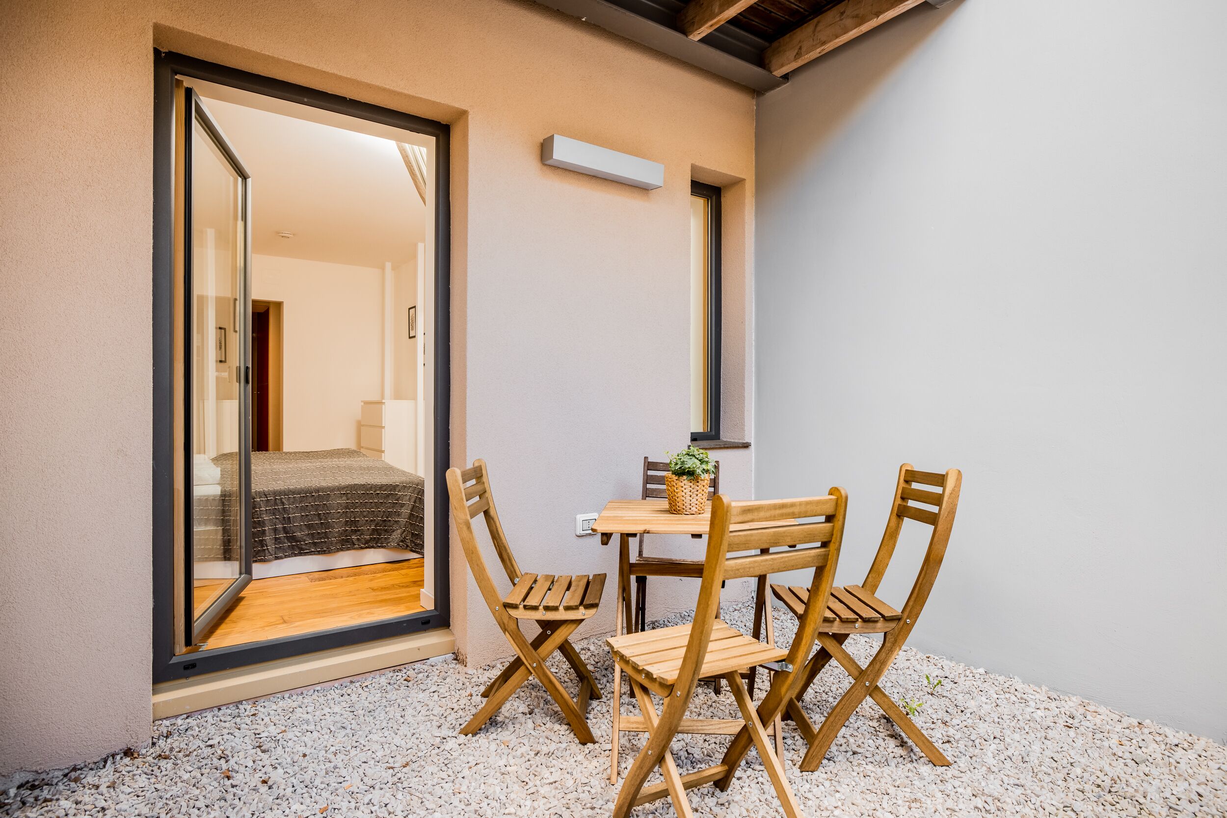 Une petite pièce comprenant un lit, une porte-fenêtre coulissante donnant sur un balcon et une table en bois avec des chaises.