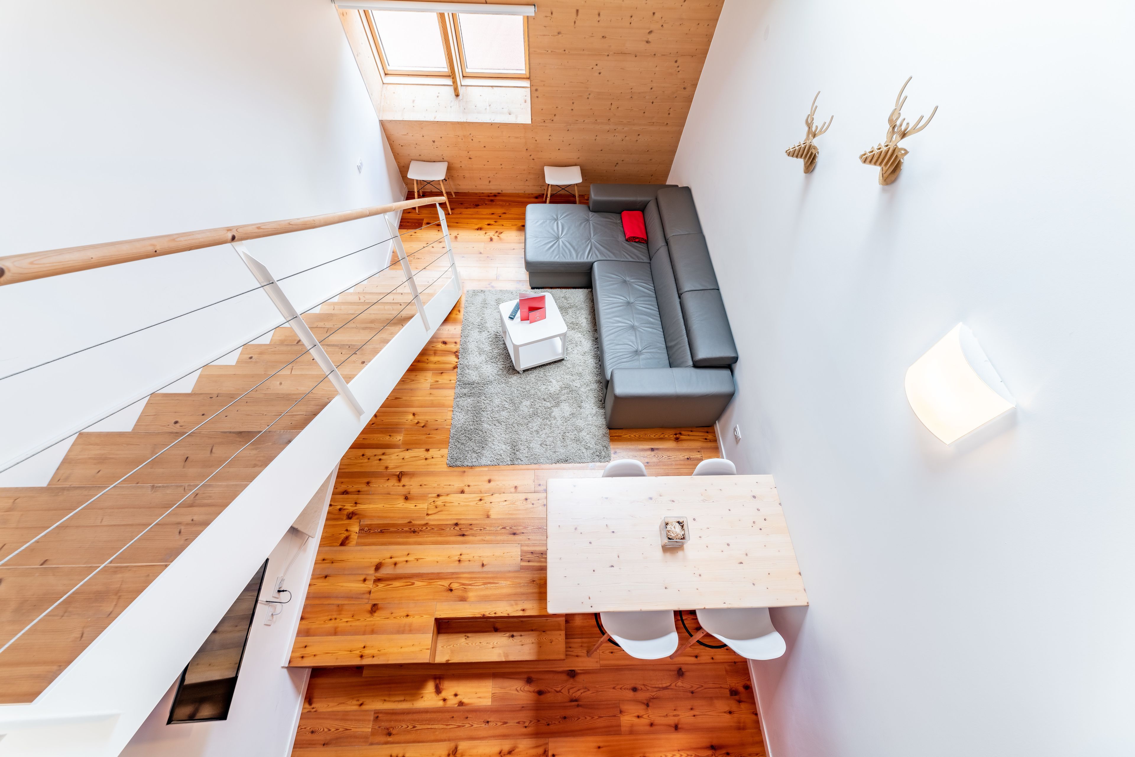 A modern loft-style living space with a wooden floor, a gray sectional sofa, a small table, and a staircase.