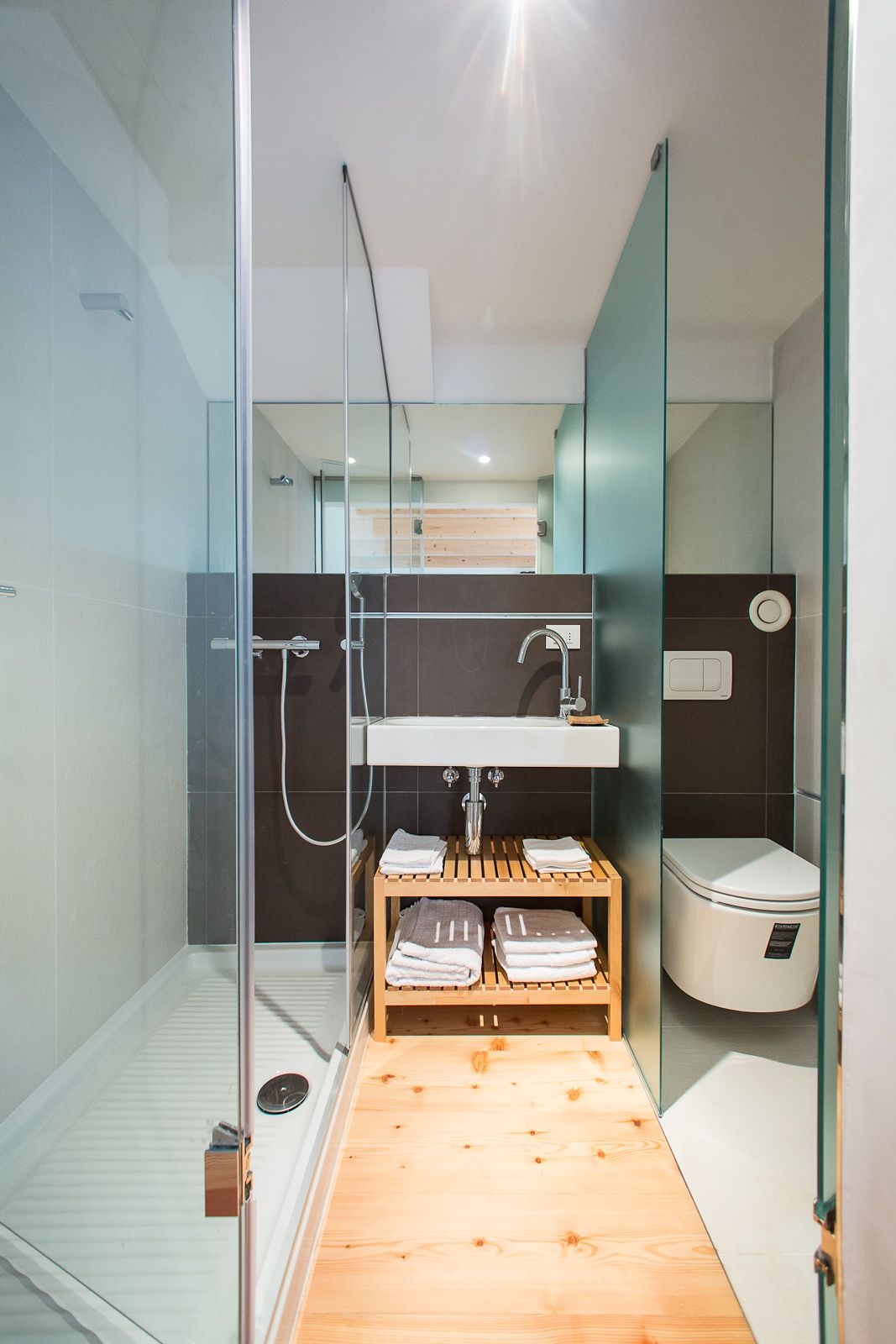 Een moderne badkamer met een douchecabine van glas, een houten wastafelmeubel en een toilet.