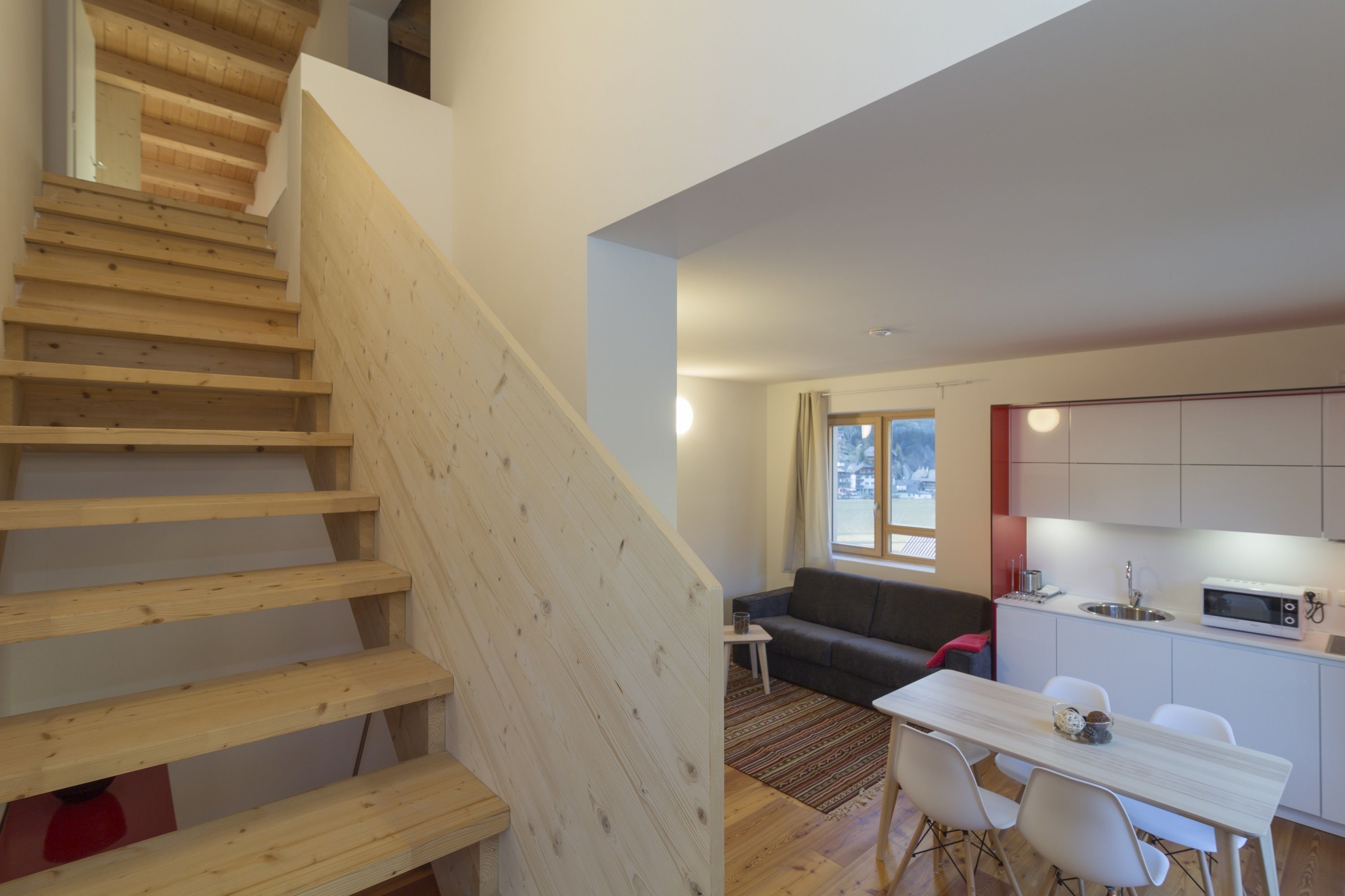 A modern interior with a wooden staircase, a dining area, a kitchen, and a living space.