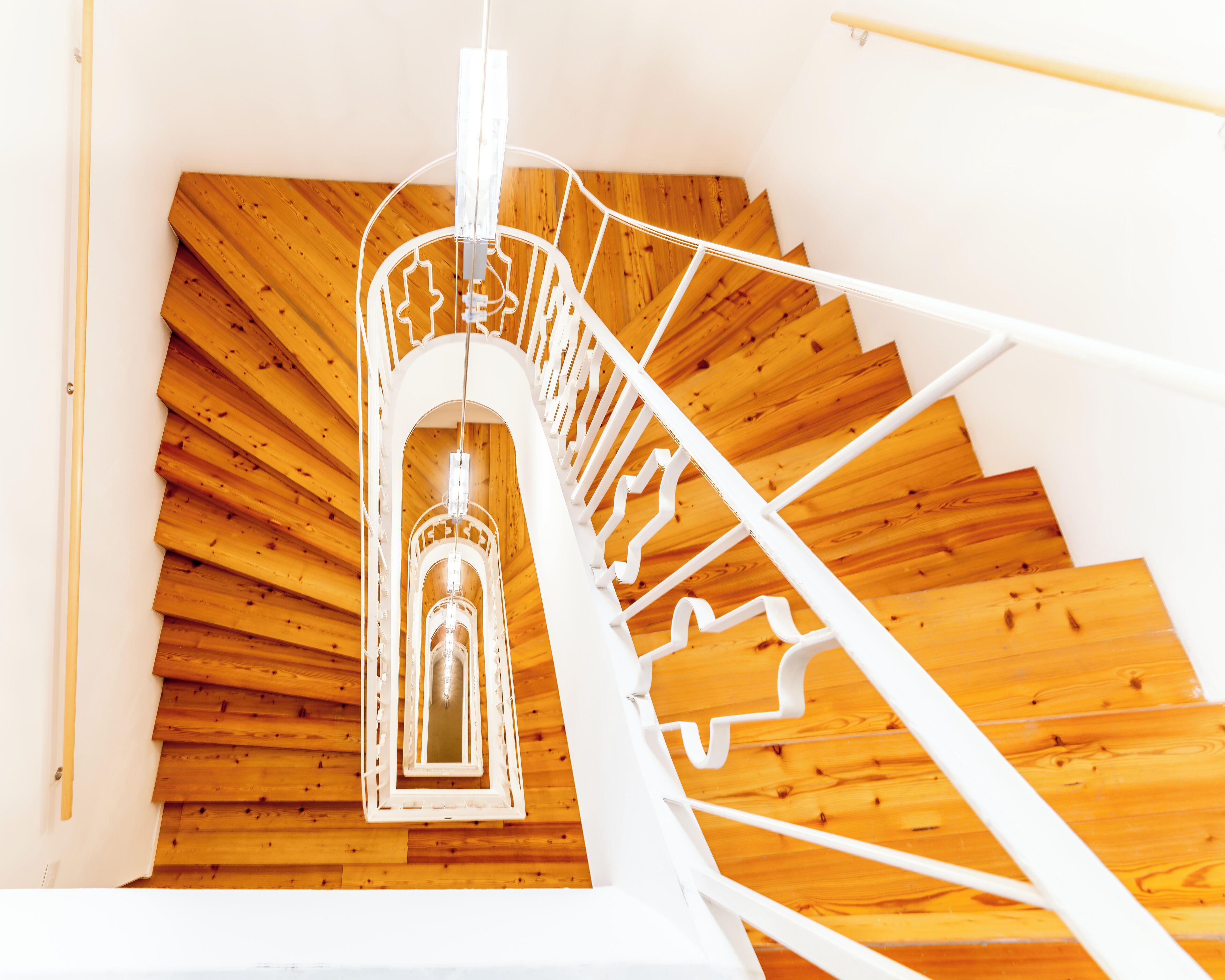 Uma escadaria em espiral com corrimão branco e degraus de madeira.