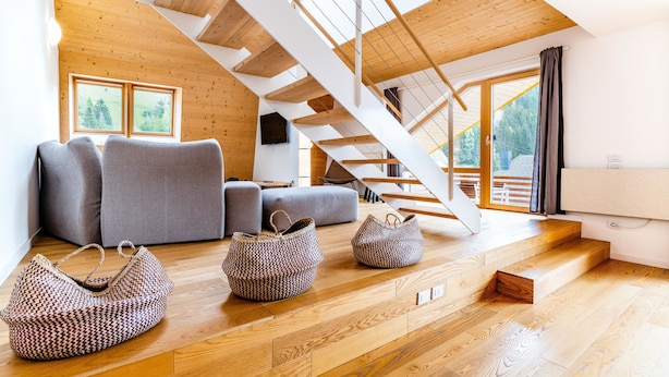 A modern interior with a wooden staircase, grey sofas, and woven baskets on a wooden floor. - Quercus Appartements (Reichenau)