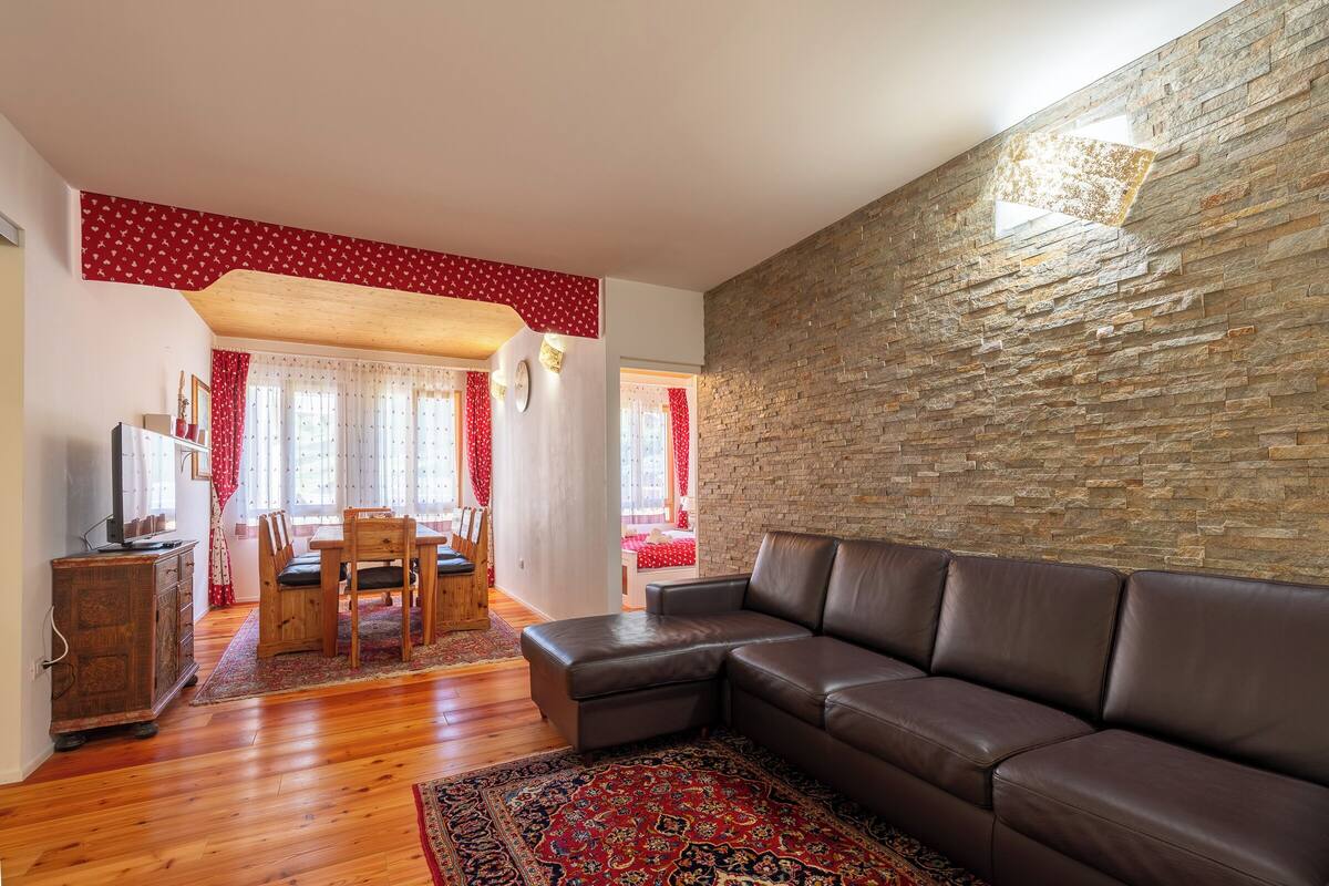 A living room with a stone wall, wooden furniture, and a red patterned rug.