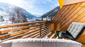 A balcony with a wooden railing, a cushioned chair, and a view of a snowy mountain landscape. - Quercus Appartements (Reichenau)