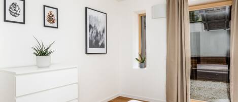 A bedroom with a bed, a white dresser, a window with curtains, and framed pictures on the wall.