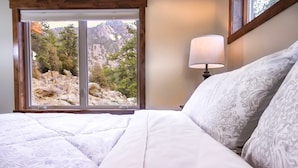 A bedroom with a large window offering a view of a mountainous landscape. - Woodlands on Fall River (Estes Park)