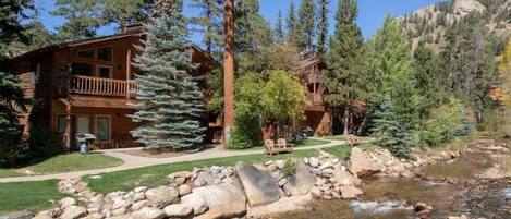 A lodge with a stone facade, a balcony with a railing, and a small stream in the foreground.