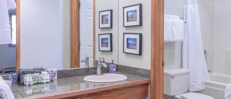 A bathroom with a wooden vanity, sink, and mirror. There are framed pictures on the wall, a shower curtain, and a toilet.