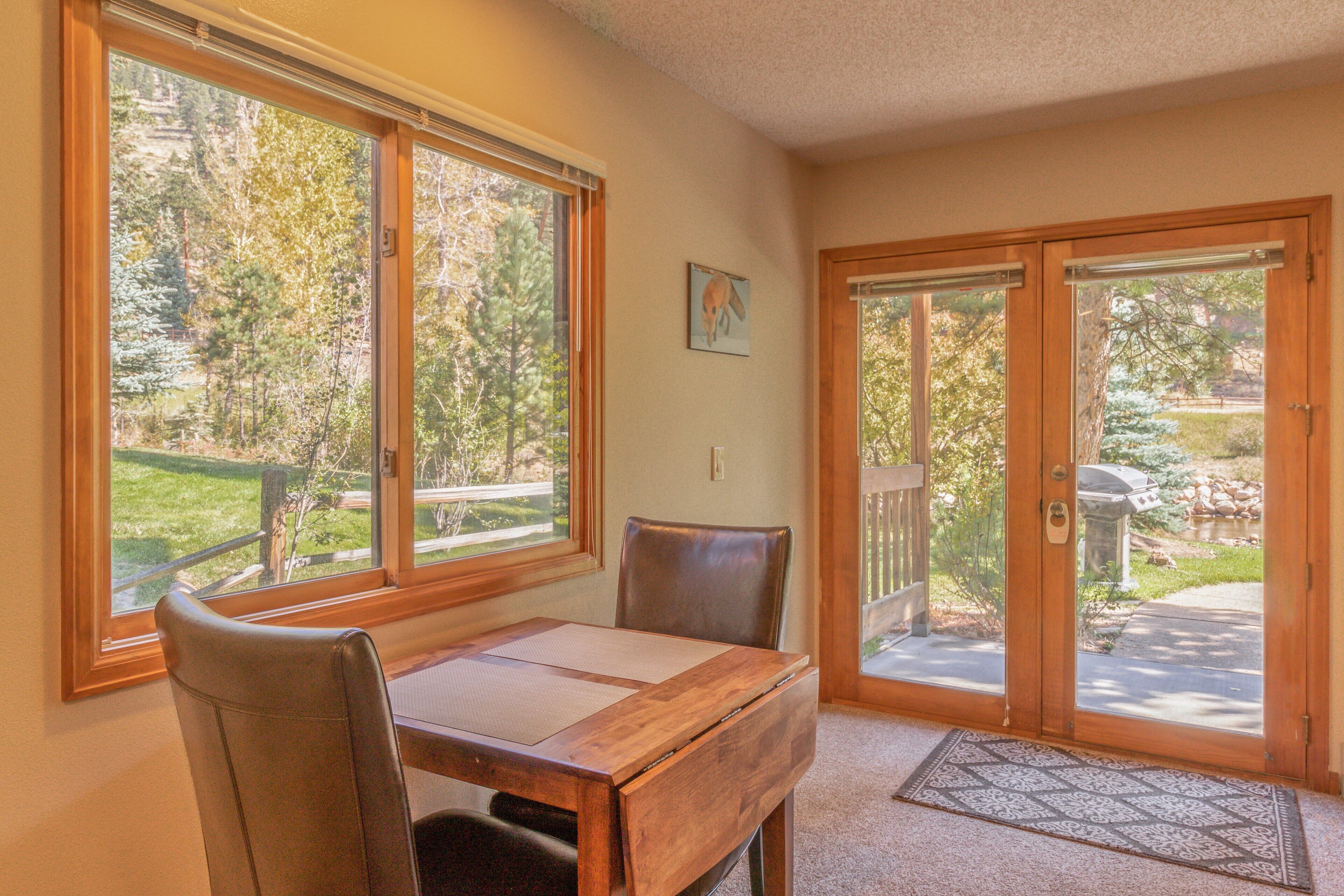 A dining area with a wooden table and chairs, large windows with a view of trees, and a sliding glass door leading to an outdoor patio.