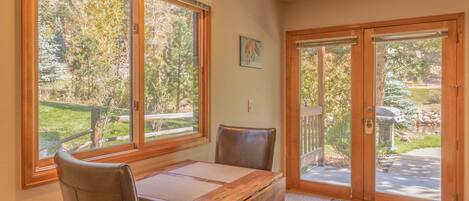 A dining area with a wooden table and chairs, large windows with a view of trees, and a sliding glass door leading to an outdoor patio.