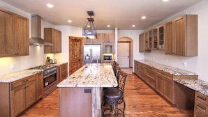 A spacious kitchen with wooden cabinets, a granite countertop, and a central island with bar stools. - Woodlands on Fall River (Estes Park)