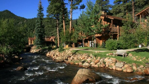 A lodge with multiple wooden cabins, a river, and a rocky shoreline. - Woodlands on Fall River (Estes Park)