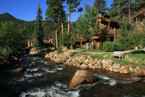A lodge with multiple wooden cabins, a river, and a rocky shoreline. - Woodlands on Fall River (Estes Park)