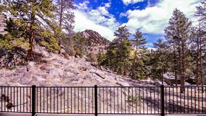 A deck with a metal railing overlooking a rocky hillside with trees. - Woodlands on Fall River (Estes Park)