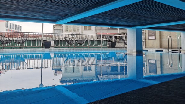 Una piscina con agua cristalina, rodeada por un borde de baldosas y barandales de metal.