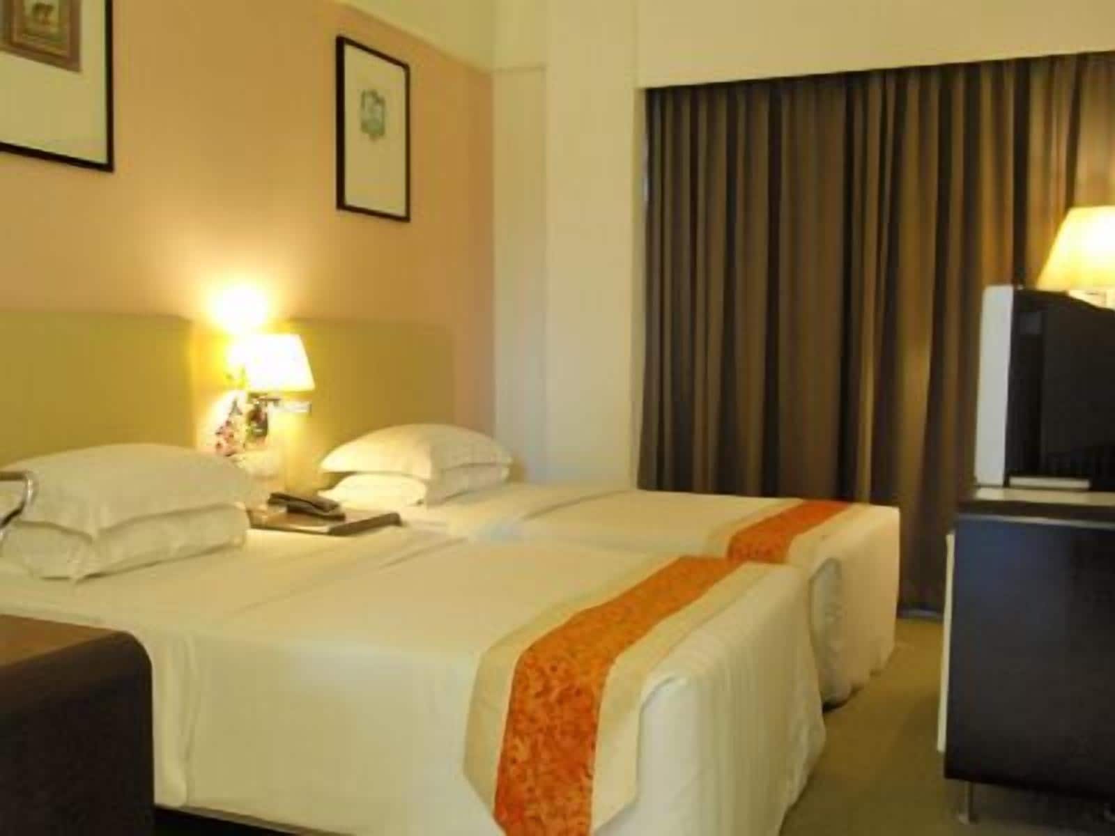 A hotel room with two beds, a nightstand, a lamp, and a large window with curtains.