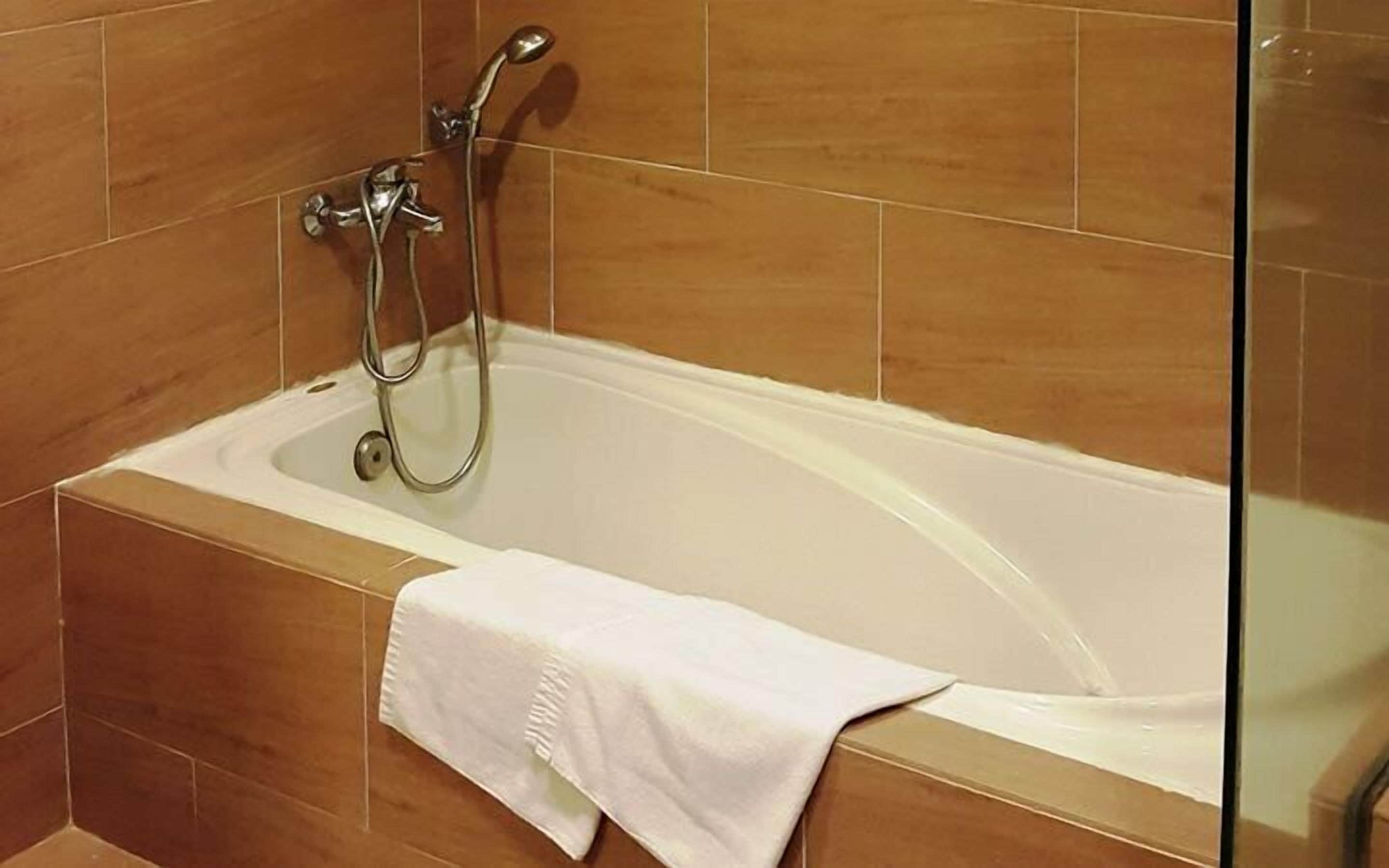 A bathtub with a shower head, a white towel, and brown tiles.