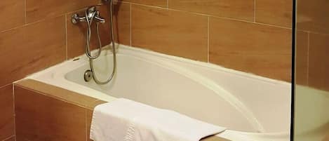 A bathtub with a shower head, a white towel, and brown tiles.