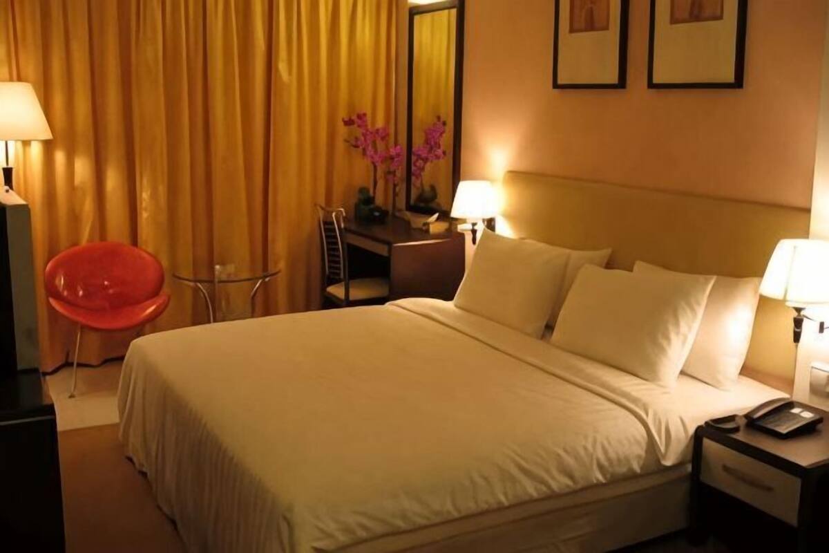 A hotel room with a bed, bedside tables, a desk, a chair, and a lamp.