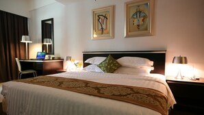 Habitación de hotel con una cama grande, un escritorio con computadora, una silla y dos cuadros en la pared.