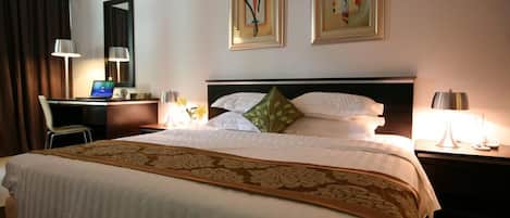 A hotel room with a large bed, a desk with a computer, a chair, and two paintings on the wall.