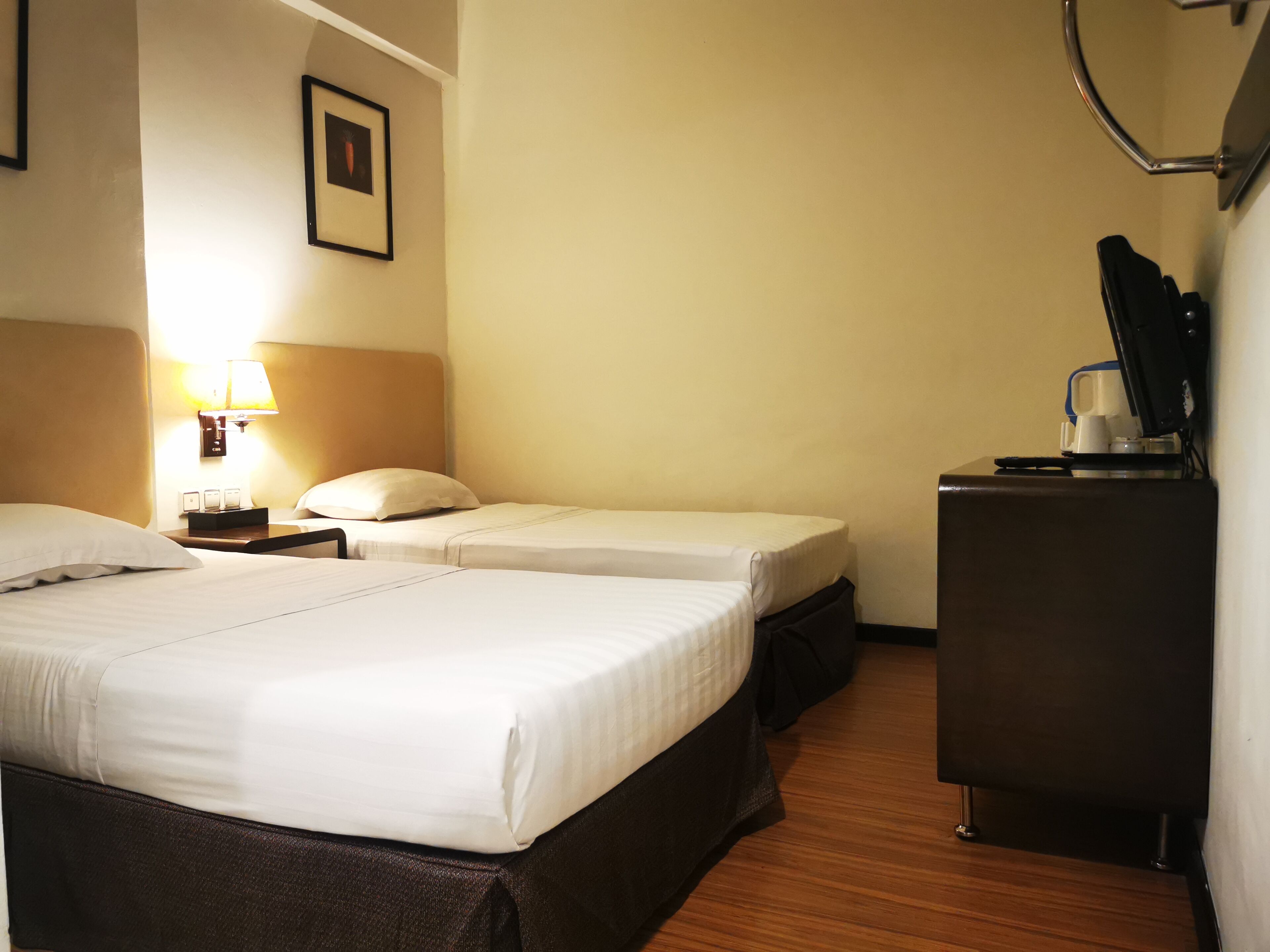 A hotel room with two beds, a desk, a lamp, and a coffee machine.