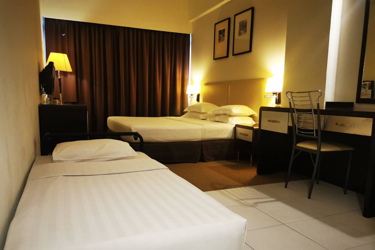 Hotellihuone, jossa on kaksi sänkyä, työpöytä, tuoli, lamppu ja verho.