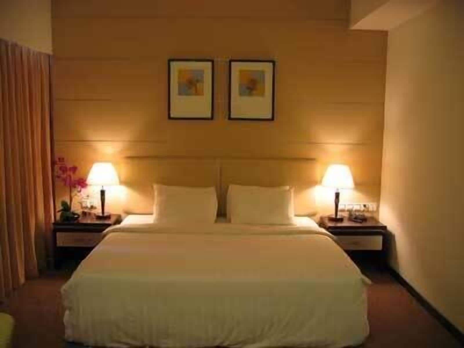A hotel room with a large bed, two bedside tables, and two lamps.