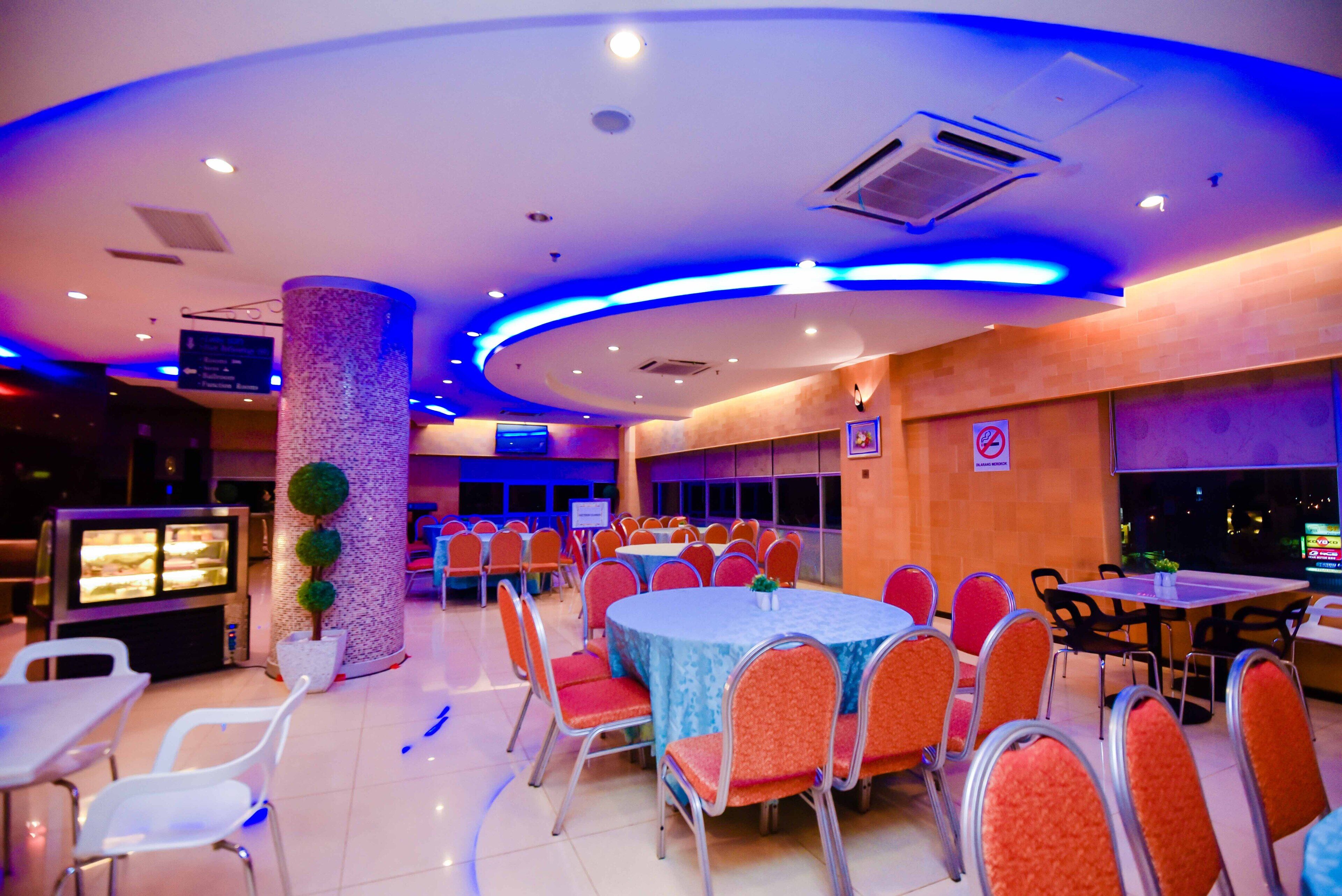 A banquet hall with round tables and orange chairs, a pillar with greenery, and a dessert display.