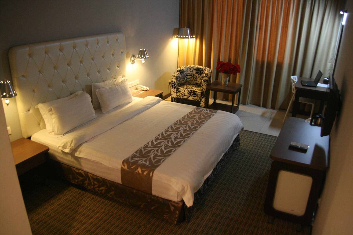 A hotel room with a large bed, a chair, a desk, and a lamp.