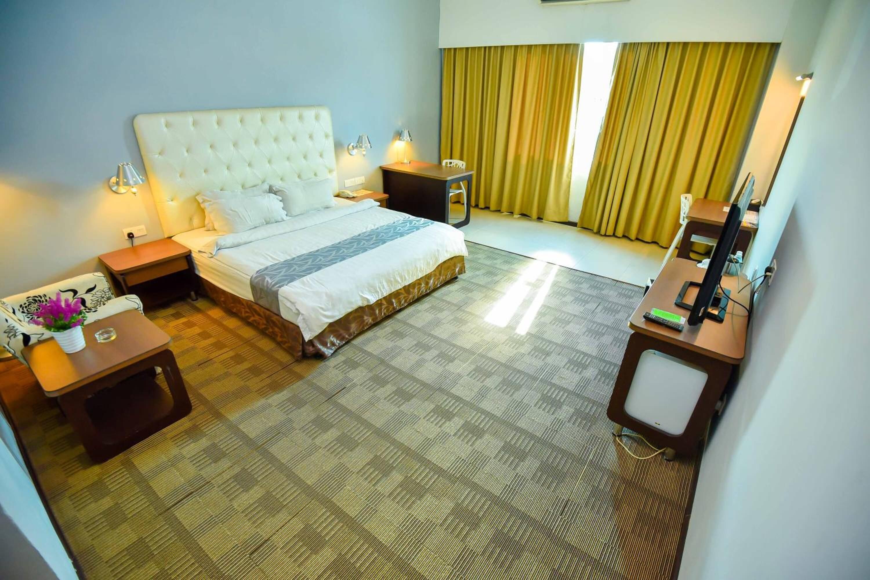 A hotel room with a large bed, bedside tables, a desk, a chair, and a television.
